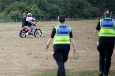 Police look on as two men on a motorbike drive away across a field