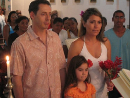 The couple stand together with the little girl in front of them and the congregation visible behind them