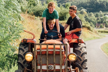 Three teenage boys riding on a tractor along a rural road