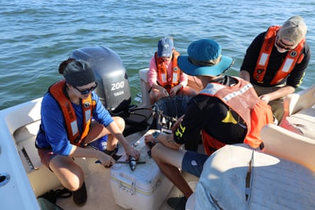 A group of people wearing lifejackets on a boat prepare mackerel bait.
