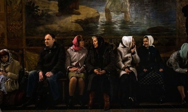 People sitting on bench in church, with women wearing headscarves.