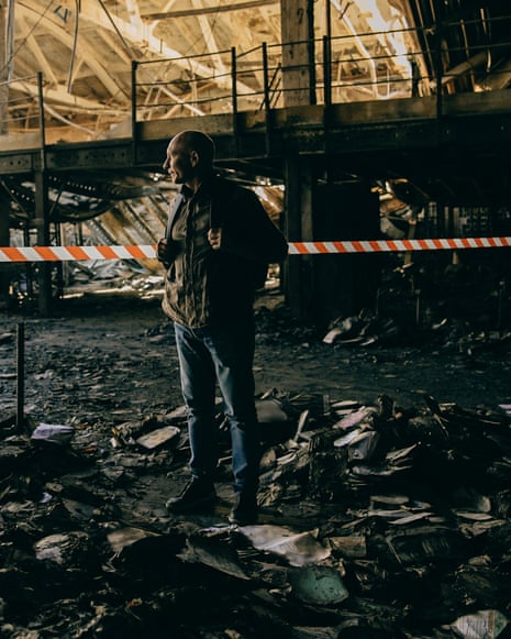 Viktor Kruglov stands amid rubble in his burnt warehouse, behind orange warning tape