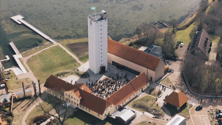 Overhead shot of a tall white grain silo next to the sea and surrounded by a courtyard filled with people and small warehouse buildings