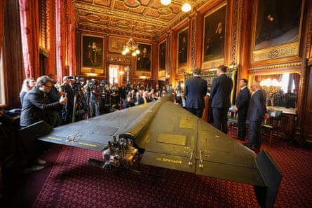 Photographers and journalists gather in an ornate Westminster room before a large metal drone