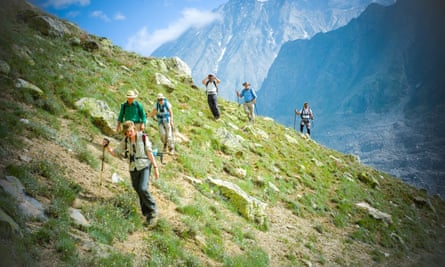 A line of trekkers on a hillside, jagged mountain peaks behind