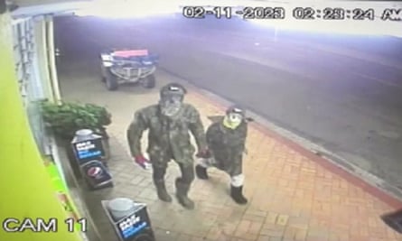 Um homem andando pela rua com roupas camufladas ao lado de uma criança, ambos usando máscaras