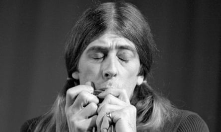 Man with long hair plays harmonica in black and white photo