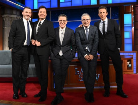 five men in black suits stand by desk