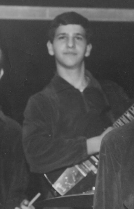 A black-and-white photo of a young man with a guitar hanging from his shoulder.