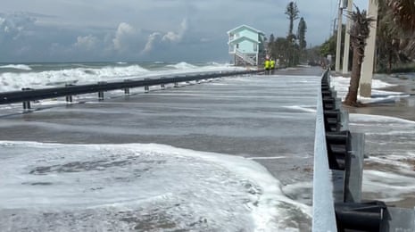 people in neon yellow jackets walk by water as large waves crash shore