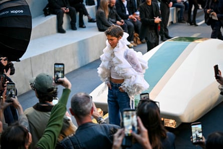 Zendaya in a flowy white jacket surrounding by press photographers.