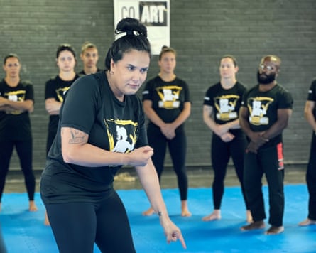 A woman stands in front of other women wearing the same T-shirt in a sports studio setting