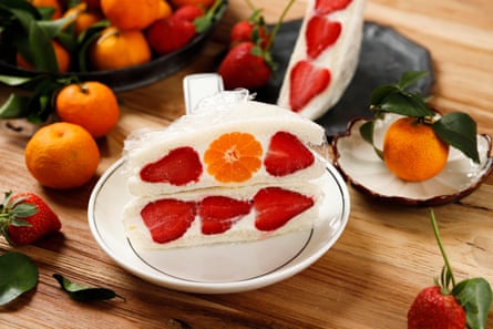 A white bread sandwich with soft cream and entire pieces of strawberry in the middle is laid on a plate in the middle of a table