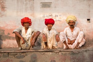 Three men sit with their back to a wall in a small village in a remote area of Rajasthan, India