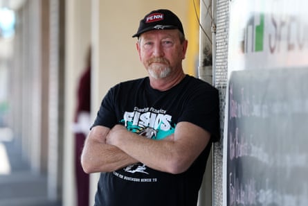 Lance Polmear, in a cap and t-shirt, leads against a wall with his arms crossed