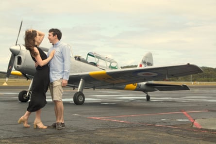 Maleah Pearce in a black dress stands next to Dylan on an airfield with a light plane behind them