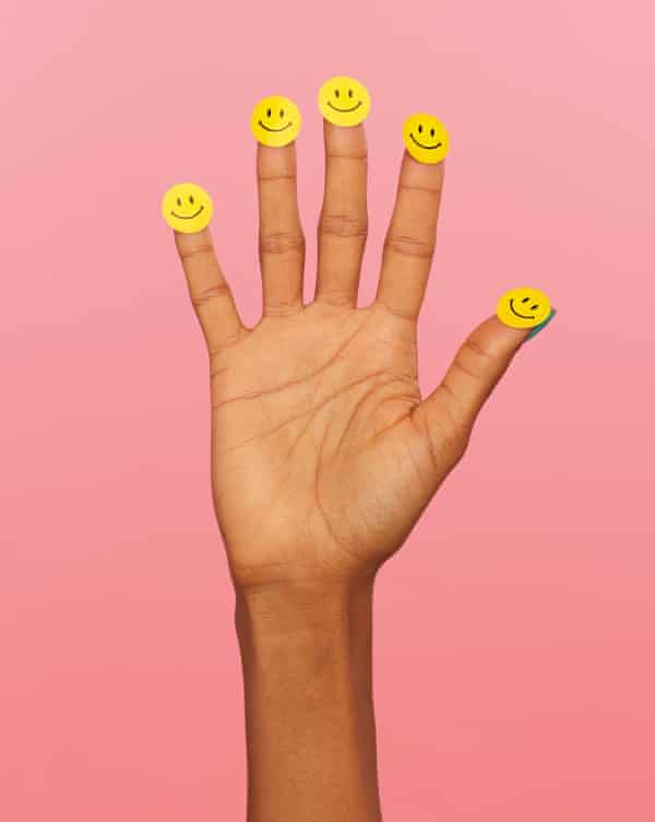 Hand with smiley stickers on fingers and thumbs, against pink background