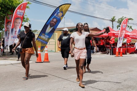 Three women smile and one raises an arm in the street in front of banners showing the candidates.
