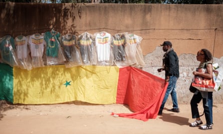 Ablaye Diaby mette una bandiera sotto dozzine di magliette da calcio su un muro di fronte al suo piccolo negozio a Dakar.