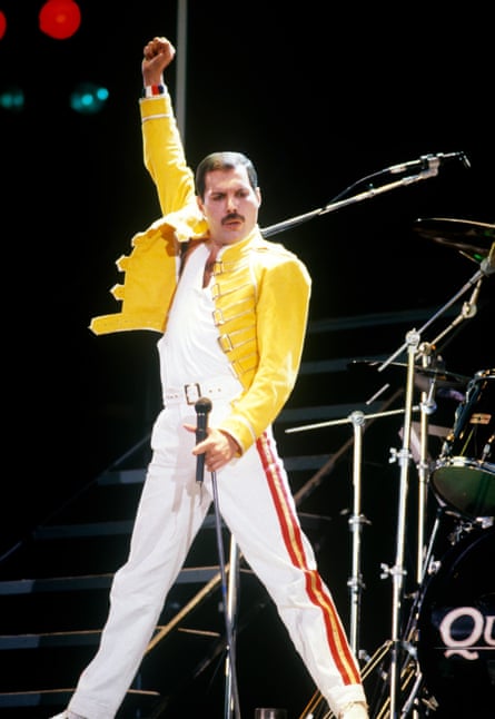 A man in a yellow jacket and white trousers and a yellow leather jacket, raising his arm in the air