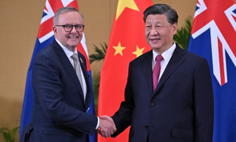 Anthony Albanese and Xi Jinping shake hands, smile and face the media in front of national flags