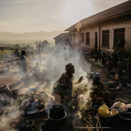 smoke rises from fires as women cook in the open