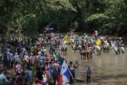 Protesters with flags and banners lead horses through a river during a demonstration