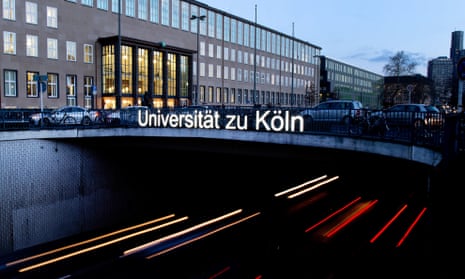 An overpass leading to an academic building with the words 'Universität zu Köln' lit up