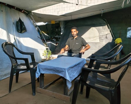 Ahmed Ishtaiwi sits in a tent at a table with a blue cloth and three black plastic chairs