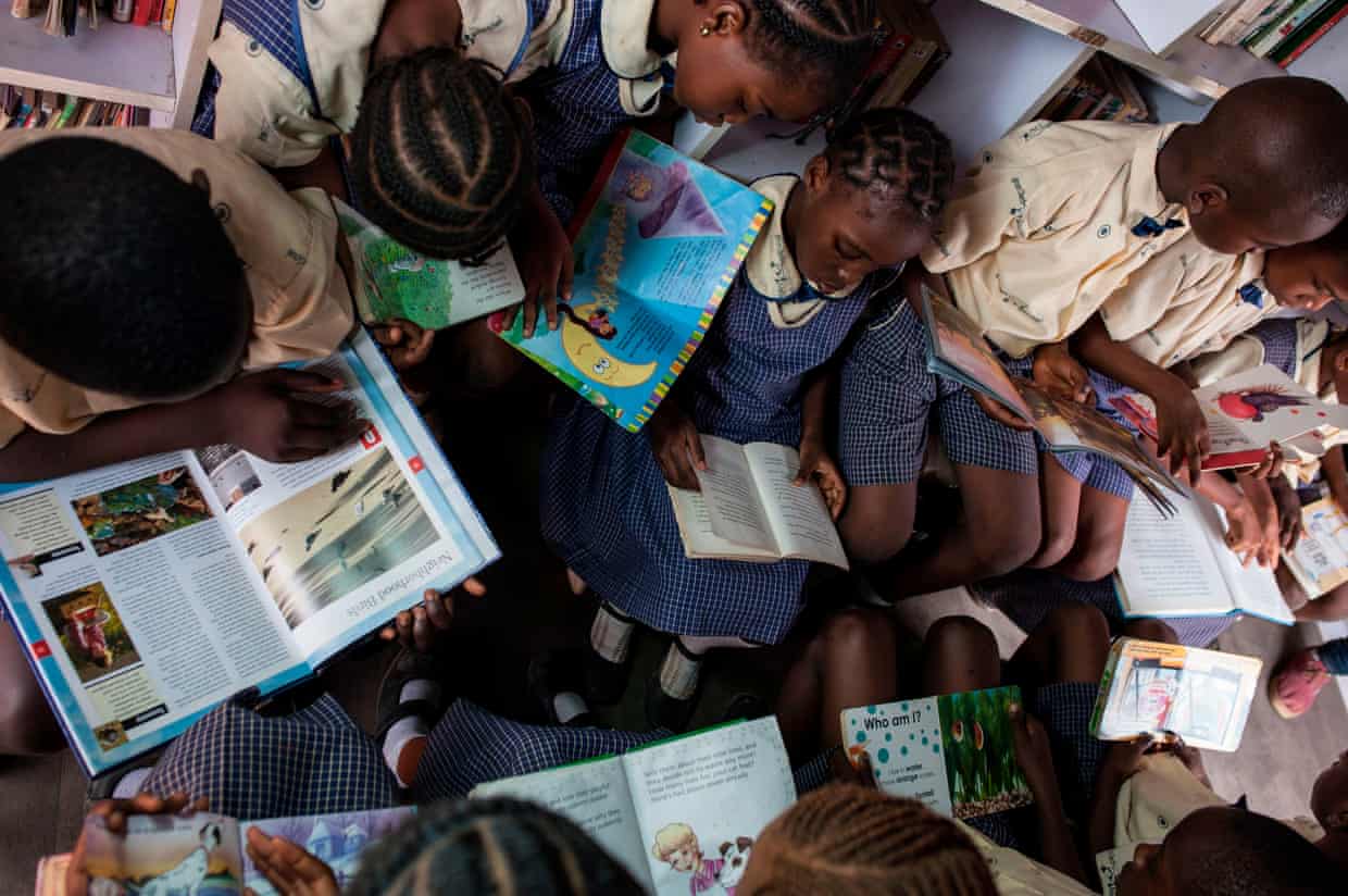 Eleven African children seen from above, all reading books while sitting in a small space