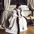 Olivia Colman, playing Queen Anne, sits on the end of a four-poster bed with extravagant curtains. She wears an elaborate ermine gown.