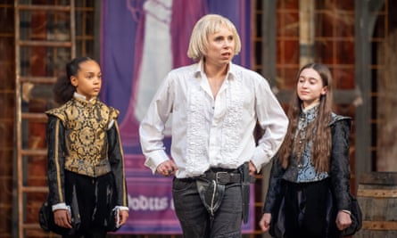 Terry on stage in character wearing a ruffled white shirt and black trousers. Two children stand behind her on stage.