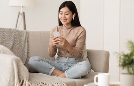 Young woman relaxes on couch at home listening to music on her phone