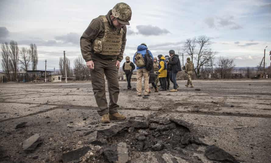 A man in military uniform looks at a shallow blast indentation on an open stretch of concrete