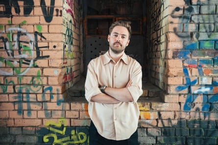 A man with folded arms standing in front of a wall, which is covered in graffiti.
