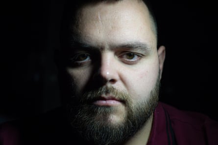 A white man with a beard and moustache. He has a scar on his forehead.