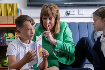 Rachel Reeves holds a finger to her lips while talking to a school boy and girl on the floor of a classroom