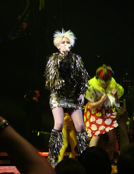 Woman wearing a gold fringed tunic dress with matching boots and white spiky wig on stage