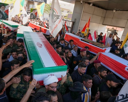 Half a dozen flag-draped coffins are carried by two columns of coffin-bearers through a covered space between a crowd of mourners