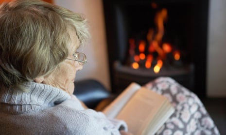 An older woman reads a book by her fire.