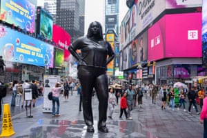 People walk past a bronze statue of a young black woman on a busy street