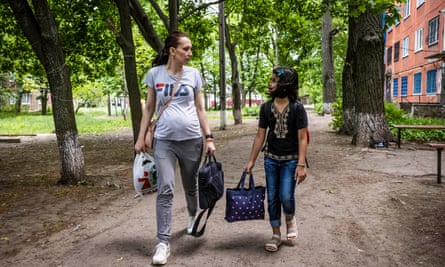 A young woman with the first signs of a baby bump talking to a young girl with her as they walk al;ong carrying bags