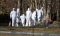 A forensics team in white overalls search a footpath in woodland