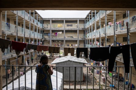 A woman stands on a balcony overlooking the internal courtyard of a building with lines of washing and other signs of