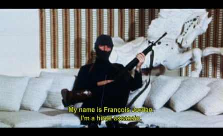 film still of a man with a balaclava holding a gun while sitting on a white sofa