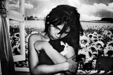 A girl with tousled hair cradles a small animal before a mural of sunflower fields
