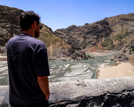 A man looking down on a river which has dried up in patches with sand showing through.