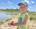 A child in bright green T-shirt smiles while holding a fishing rod by water