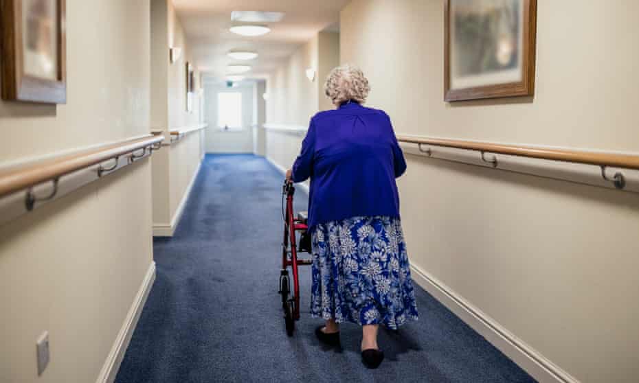 A senior woman walking down a corridor with the assistance of a walker viewed from rear