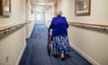 Senior Woman with Walker in a Care Home<br>A senior woman walking down a corridor with the assistance of a walker. view from rear